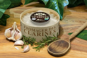 Cheese wheel from 'Fromager des Clarines' vacherin Mont D'or style on a wooden board with garlic and herbs.