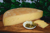 Raclette Cheese Wheel on a cheeseboard. Half a wheel and slices with cornichons and pickles.